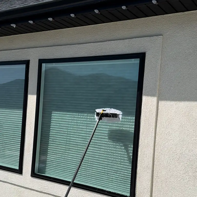 Brush tool cleaning large windows on a stucco wall, with mountain reflections in the glass.