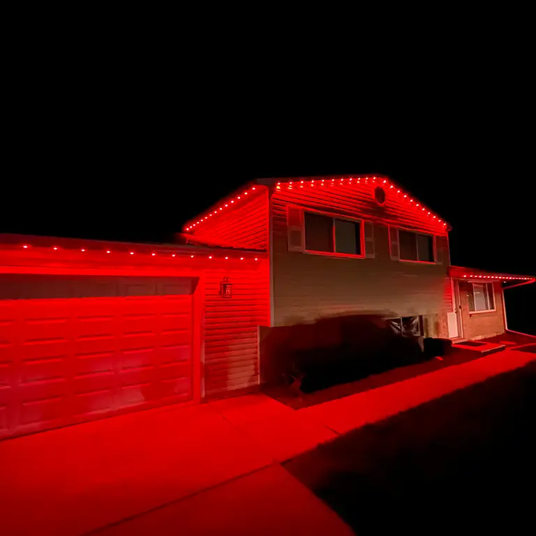 A split-level house illuminated with bold red lights along the roofline and garage at night.