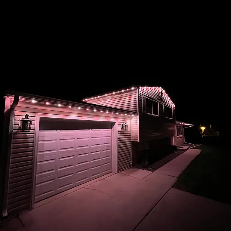 House outlined with soft pink lights, illuminating the garage and driveway at night.