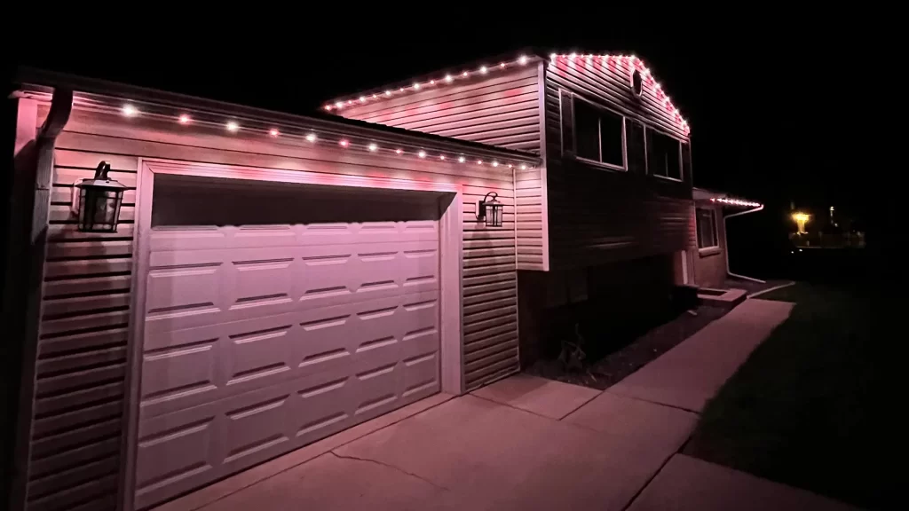 House outlined with soft pink lights, illuminating the garage and driveway at night.