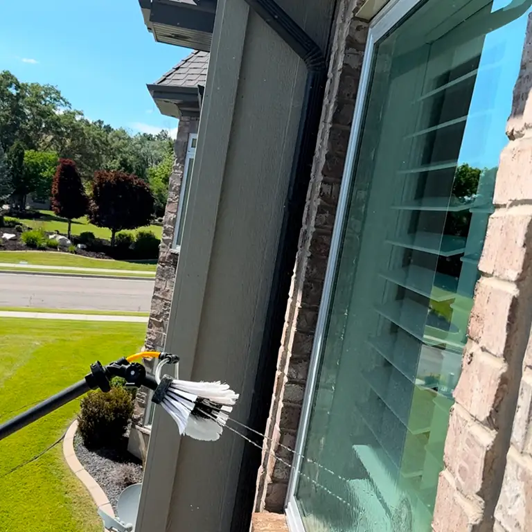 Brush attachment spraying water to clean a glass window on a stone building exterior.