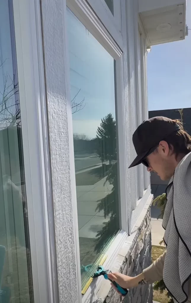 Person cleaning the edge of a glass window with a squeegee on a sunny day.