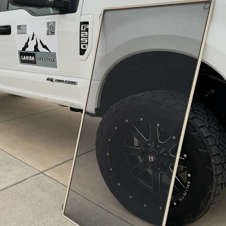 Window screen leaning against a white truck with a "Lavish Lifestyle" logo and large black tire.