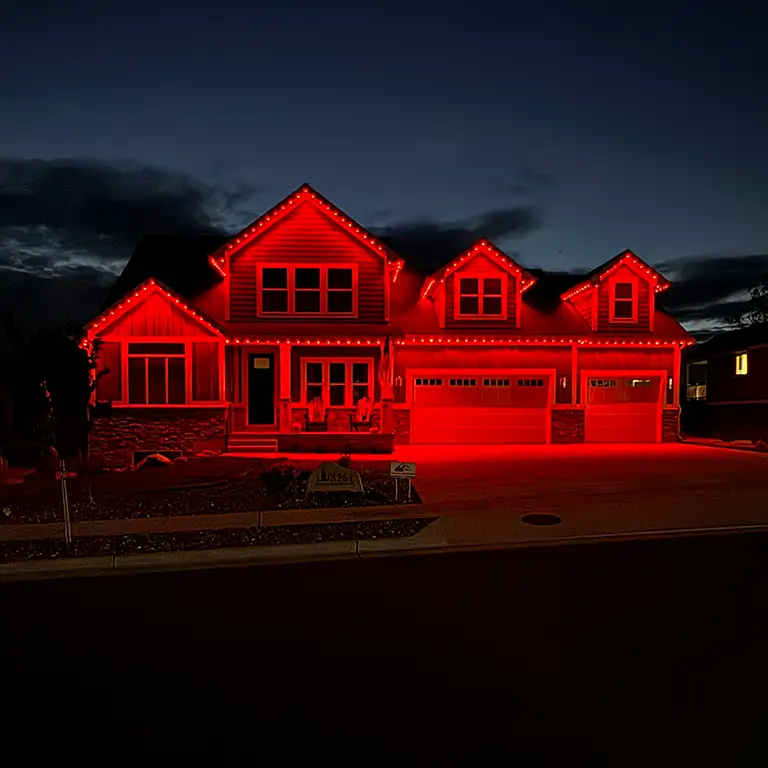 A two-story suburban house illuminated by vibrant red exterior lighting at night, highlighting its trim, windows, and garage doors.