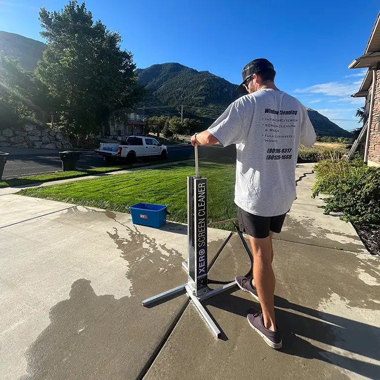 Person using a Xero screen cleaner on a driveway with mountains and trees in the background.